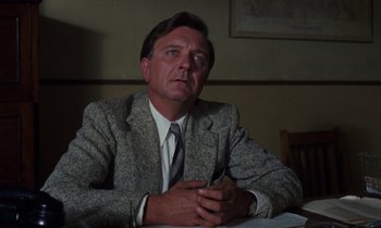 Movie still from “10 Rillington Place” (1971), directed by Richard Fleischer – A man sitting at a table in front of papers; Close Up shot, Low angle