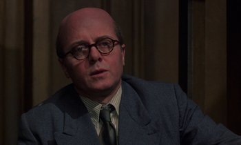 Movie still from “10 Rillington Place” (1971), directed by Richard Fleischer – A man in a suit and tie wearing glasses; Close Up shot, Over the shoulder angle