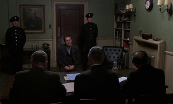 Movie still from “10 Rillington Place” (1971), directed by Richard Fleischer – A group of men sitting around a table in a room; Wide shot, Over the shoulder angle