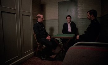 Movie still from “10 Rillington Place” (1971), directed by Richard Fleischer – Two men sitting at a table in front of a door; Wide shot, High angle