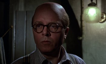 Movie still from “10 Rillington Place” (1971), directed by Richard Fleischer – A bald man wearing glasses and a striped shirt; Close Up shot, Over the shoulder angle