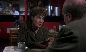 Movie still from “10 Rillington Place” (1971), directed by Richard Fleischer – An older woman sitting at a table with a cup of coffee; Medium shot, Over the shoulder angle