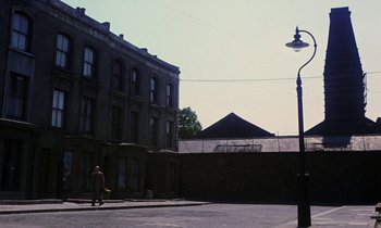 Movie still from “10 Rillington Place” (1971), directed by Richard Fleischer – A person walking down a street near a building; Extreme Wide shot, Low angle