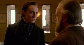 Movie still from “Crimson Peak” (2015), directed by Guillermo del Toro – A man standing next to another man in a room; Medium shot, Over the shoulder angle