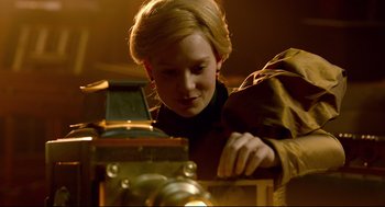 Movie still from “Crimson Peak” (2015), directed by Guillermo del Toro – A young girl looking at a camera in a dimly - lit room; Close Up shot, Low angle