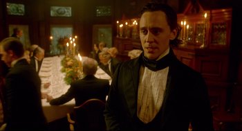 Movie still from “Crimson Peak” (2015), directed by Guillermo del Toro – A man standing in front of a group of people in a room; Medium shot, Over the shoulder angle