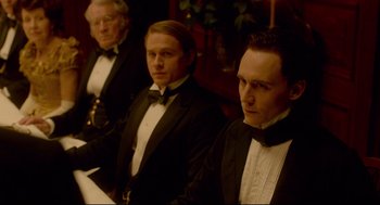 Movie still from “Crimson Peak” (2015), directed by Guillermo del Toro – A group of men in tuxedos sitting next to each other; Medium shot, Over the shoulder angle