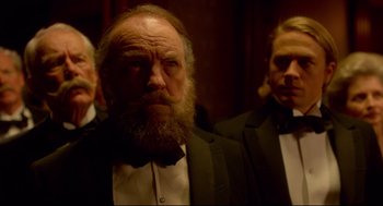 Movie still from “Crimson Peak” (2015), directed by Guillermo del Toro – A man with a long beard wearing a suit and bow tie; Close Up shot, Low angle