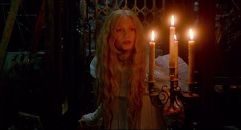 Movie still from “Crimson Peak” (2015), directed by Guillermo del Toro – A woman with long blonde hair standing next to two lit candles; Medium shot, Low angle
