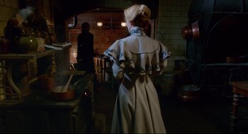 Movie still from “Crimson Peak” (2015), directed by Guillermo del Toro – A woman wearing a long coat standing next to a stove; Medium shot, Over the shoulder angle
