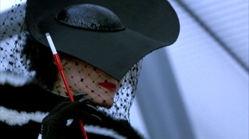 Movie still from “101 Dalmatians” (1996), directed by Stephen Herek – A woman wearing a black hat and holding a red umbrella; Extreme Close Up shot, Low angle