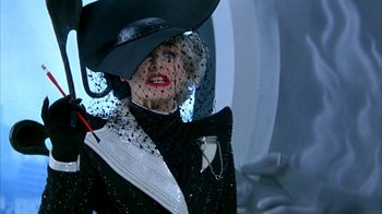 Movie still from “101 Dalmatians” (1996), directed by Stephen Herek – A woman wearing a black hat and a black suit; Close Up shot, Over the shoulder angle