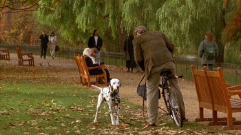 Movie still from “101 Dalmatians” (1996), directed by Stephen Herek – A man on a bicycle with a dog in a park; Wide shot, Over the shoulder angle