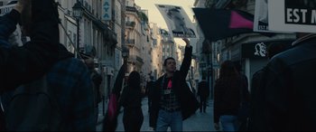 Movie still from “120 BPM” (2017), directed by Robin Campillo – A man holding up a protest sign in the middle of a crowded street; Medium shot, Low angle