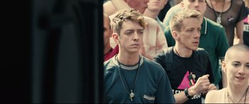 Movie still from “120 BPM” (2017), directed by Robin Campillo – A young man with a cross on his neck and a crowd of people behind him; Close Up shot, High angle
