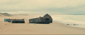 Movie still from “120 BPM” (2017), directed by Robin Campillo – Two people walking on the beach near a large rock; Extreme Wide shot, High angle