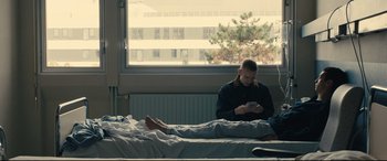 Movie still from “120 BPM” (2017), directed by Robin Campillo – A man sitting on a bed looking at his cell phone; Wide shot, Low angle