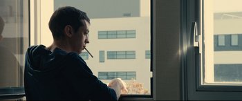 Movie still from “120 BPM” (2017), directed by Robin Campillo – A man sitting at a window with a cigarette in his mouth; Medium shot, Low angle
