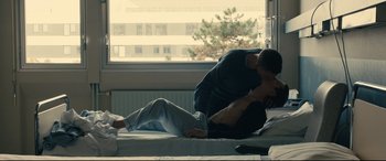 Movie still from “120 BPM” (2017), directed by Robin Campillo – A man laying on a bed with another man standing next to him; Medium shot, Overhead angle