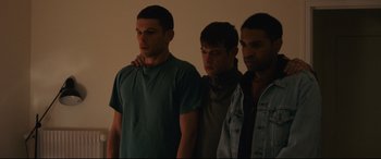 Movie still from “120 BPM” (2017), directed by Robin Campillo – Three young men standing next to each other in front of a white wall; Medium shot, Low angle