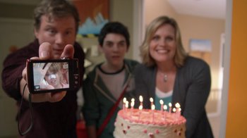 Movie still from “16 Wishes” (2010), directed by Peter DeLuise – A woman standing next to a cake with candles on it; Medium shot, Over the shoulder angle