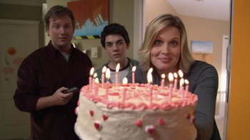 Movie still from “16 Wishes” (2010), directed by Peter DeLuise – A woman and two men standing in front of a birthday cake; Medium shot, Over the shoulder angle