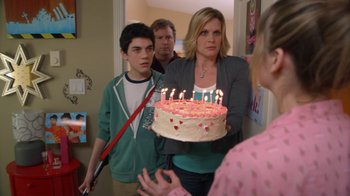 Movie still from “16 Wishes” (2010), directed by Peter DeLuise – A woman is holding a birthday cake in front of a group of people; Medium shot, Over the shoulder angle