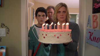Movie still from “16 Wishes” (2010), directed by Peter DeLuise – A woman holding a birthday cake in front of two men; Medium shot, Over the shoulder angle