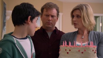 Movie still from “16 Wishes” (2010), directed by Peter DeLuise – A man and a woman and a boy standing next to a birthday cake; Close Up shot, Over the shoulder angle