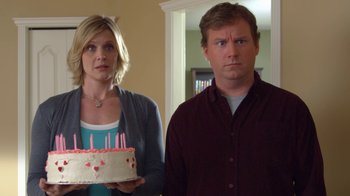 Movie still from “16 Wishes” (2010), directed by Peter DeLuise – A man and a woman standing next to each other holding a birthday cake; Medium shot, Over the shoulder angle