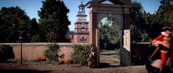 Movie still from “1776” (1972), directed by Peter H. Hunt – A woman standing in front of an archway in front of a building; Extreme Wide shot, Low angle