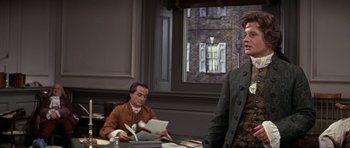 Movie still from “1776” (1972), directed by Peter H. Hunt – A man standing in front of another man holding papers; Medium shot, Over the shoulder angle