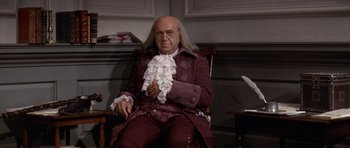 Movie still from “1776” (1972), directed by Peter H. Hunt – An old man sitting in a chair in a room; Medium shot, High angle