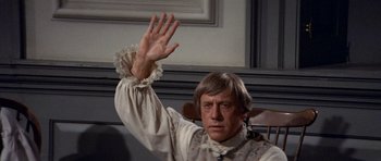 Movie still from “1776” (1972), directed by Peter H. Hunt – A man in a white shirt and a brown vest is holding his hand up in the air; Medium shot, High angle