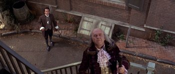Movie still from “1776” (1972), directed by Peter H. Hunt – A man dressed as ben franklin standing on a porch; Wide shot, High angle