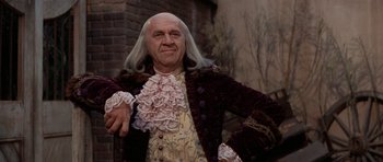 Movie still from “1776” (1972), directed by Peter H. Hunt – A man dressed as benjamin franklin posing for a picture; Medium shot, Low angle