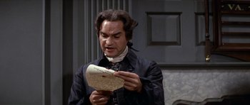 Movie still from “1776” (1972), directed by Peter H. Hunt – A man holding a piece of paper in front of a wall; Medium shot, High angle