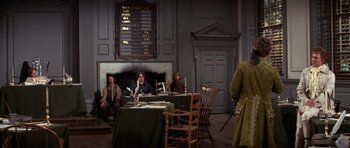 Movie still from “1776” (1972), directed by Peter H. Hunt – A group of people sitting at a table in front of a fireplace; Wide shot, Over the shoulder angle