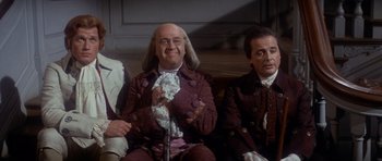 Movie still from “1776” (1972), directed by Peter H. Hunt – A group of men sitting next to each other on top of a bench; Medium shot, High angle