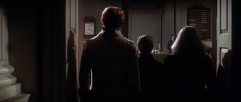 Movie still from “1776” (1972), directed by Peter H. Hunt – A group of people standing in a dark room; Wide shot, Over the shoulder angle