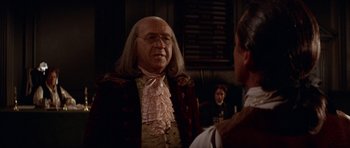 Movie still from “1776” (1972), directed by Peter H. Hunt – A man in a wig and a wig stands next to another man in a suit; Close Up shot, Over the shoulder angle