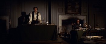 Movie still from “1776” (1972), directed by Peter H. Hunt – A man standing in front of a dining room table; Wide shot, Over the shoulder angle