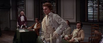 Movie still from “1776” (1972), directed by Peter H. Hunt – A man standing in front of a group of people; Medium shot, Over the shoulder angle