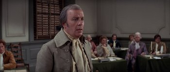 Movie still from “1776” (1972), directed by Peter H. Hunt – An older man is standing in front of a group of people; Medium shot, Over the shoulder angle