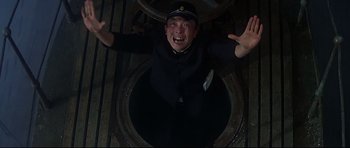 Movie still from “1941” (1979), directed by Steven Spielberg – A man in a black suit and a black hat is standing in a hole in the ground; Medium shot, Overhead angle
