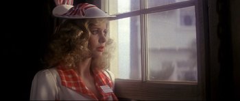 Movie still from “1941” (1979), directed by Steven Spielberg – A woman in a hat and a red and white checkered shirt looking out of a window; Close Up shot, Over the shoulder angle