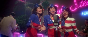 A couple of women singing into microphones in front of neon lights