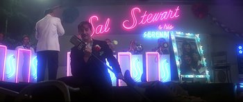 Movie still from “1941” (1979), directed by Steven Spielberg – A man in a suit and tie holding a microphone in front of a neon sign; Wide shot, Low angle