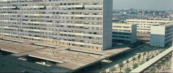 Movie still from “2 or 3 Things I Know About Her” (1967), directed by Jean-Luc Godard – An aerial view of a building with a parking lot in the foreground; Extreme Wide shot, High angle