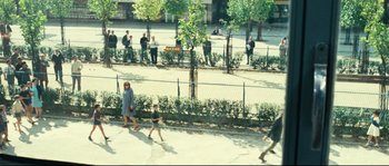 Movie still from “2 or 3 Things I Know About Her” (1967), directed by Jean-Luc Godard – A group of people walking down a sidewalk near a fence; Extreme Wide shot, High angle
